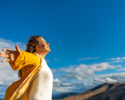 A woman stands with her arms spread wide, staring at the sky.