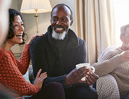 A group of adults in cozy sweaters sit together, talking and laughing. 