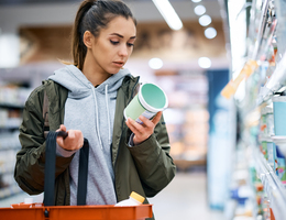 A woman reads information on a jar of food in a grocery store.