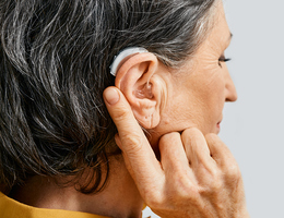 A woman points to her hearing aid.