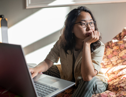 A woman sitting in front of a laptop but staring to the side.