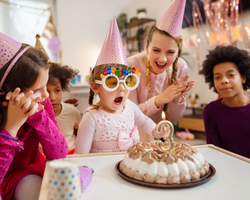 A girl blows out a birthday candle shaped like a 3 as friends watch.