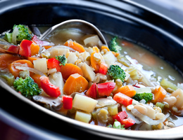 Close-up of a ladle and a slow cooker full of stew.