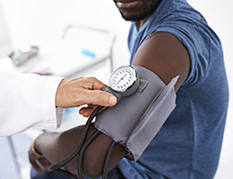 Close-up of a blood pressure cuff on a patient's arm with a provider's hand nearby. 