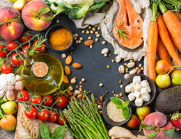 A table with various fruits, vegetables, nuts, seeds, herbs, spices, bread, fish, oil and cheese.