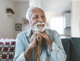 A seated man rests his hands and chin on top of a cane