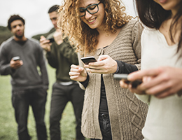 A group of teens standing around all looking at their phones. 