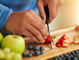 Hands slice strawberries on a cutting board.