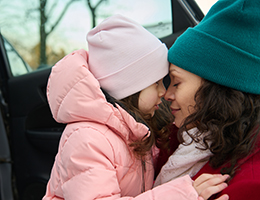 A woman rubs noses with a young girl next to an open car door.