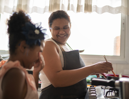 Woman stirring a pot on a stove while sharing a laugh with a girl.