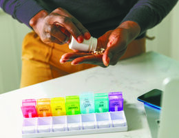 Hands shake pills from a bottle to place in a weekly organizer.