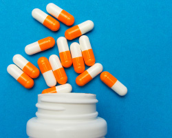 Orange and white capsules spill from a white pill bottle.