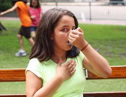 A girl uses an inhaler outdoors.