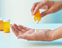 A person pours white tablets from a prescription bottle into their palm.