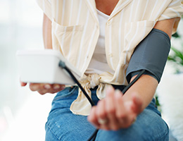 A woman sitting down taking her blood pressure at home.