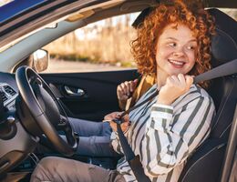 A woman fastens her seat belt, driver’s door still open.