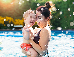 A woman holds a child in a pool. 