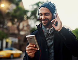 A man wearing headphones smiles at his smartphone.