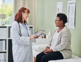 A doctor talks to a woman who is seated on an exam table.